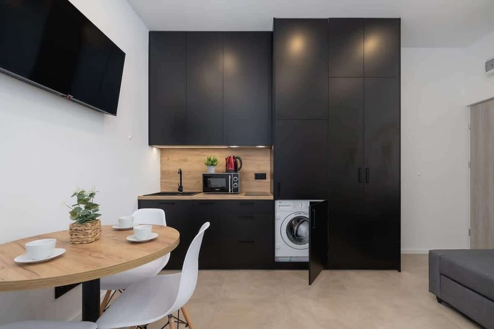 A compact, elegant dining area with a round wooden table and two chairs, seamlessly integrated into the minimalist black kitchen design.
