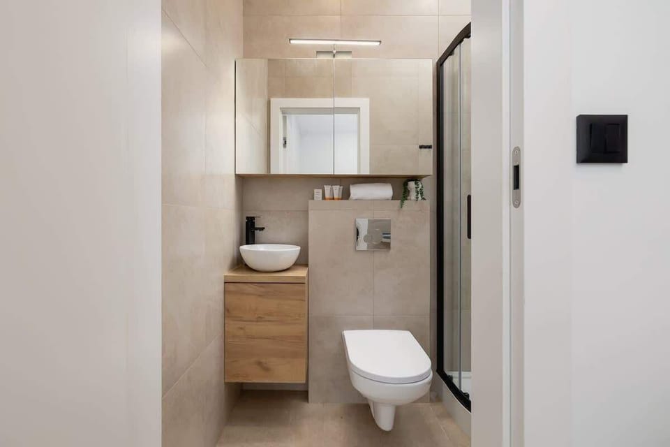 A modern bathroom with a glass-enclosed shower, black fixtures, and a stylish round mirror, creating a sophisticated ambiance.






