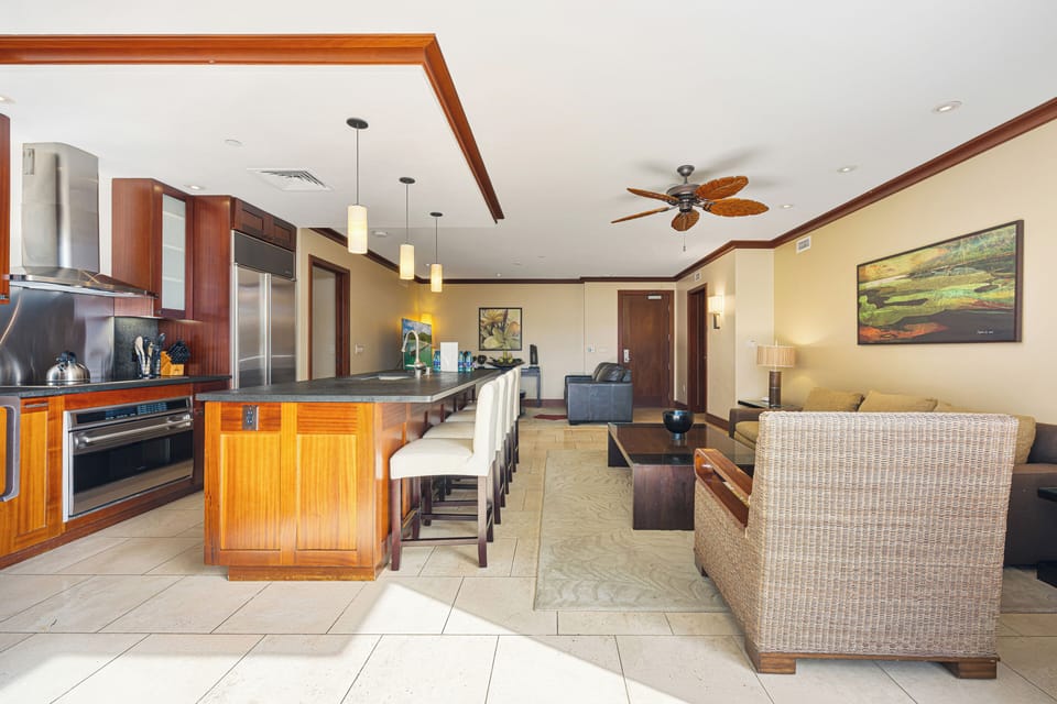 Relax in your spacious open-plan living area featuring a fully equipped gourmet kitchen, elegant dining bar with seating for six, and a comfortable lounge space with tropical ceiling fan.