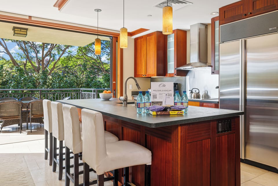 Picture yourself preparing meals in this gourmet kitchen with elegant wood cabinetry, stainless steel appliances, and a breakfast island—all opening to lush tropical views beyond.