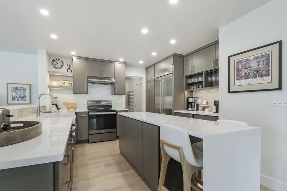 Your modern kitchen features sleek gray cabinetry, gleaming white countertops, and stainless steel appliances. Prepare meals with ease at the spacious island, surrounded by tasteful artwork and warm lighting.