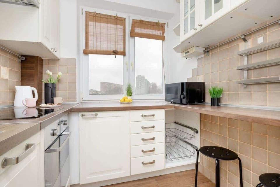 Another angle of the charming kitchen, showcasing open wooden shelves, a cozy window with natural light, and a functional countertop.


