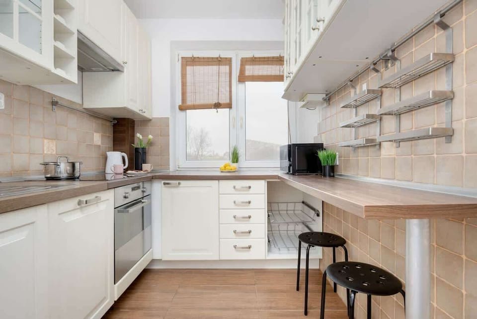 A compact yet charming kitchen with white cabinetry, open wooden shelves, and a dark wood countertop, giving it a rustic-modern appeal.

