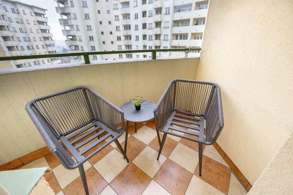 A charming balcony with a tiled floor, two cozy chairs, and a small table, perfect for enjoying a morning coffee with a city view.
