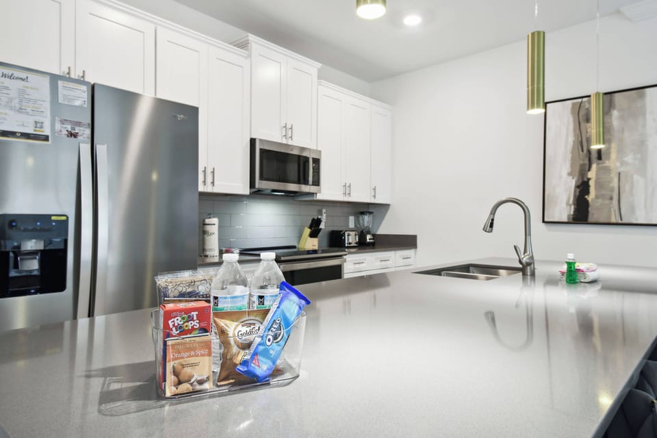 The sleek kitchen features a spacious quartz island perfect for meal prep or dining, along with stainless steel appliances and bright white cabinetry, combining modern style with functionality to inspire your culinary creativity.