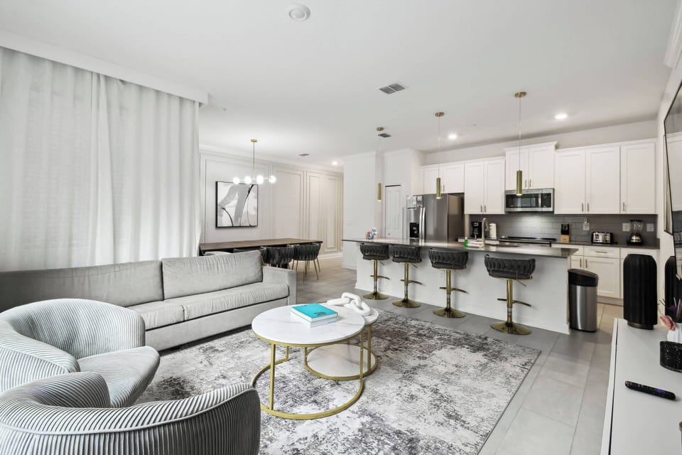 Enjoy contemporary comfort in this spacious living area with plush grey seating and a stylish round coffee table on a soft rug. The sleek kitchen, with modern bar stools, is ideal for casual dining and entertaining.