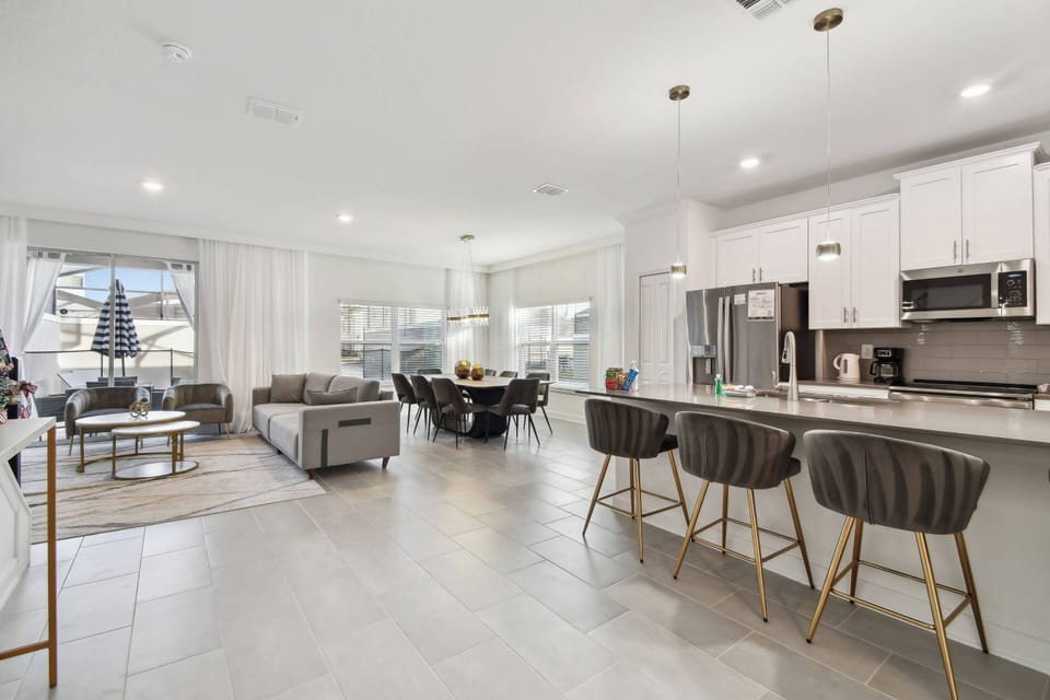 Unwind in the open living area with sleek gray cabinetry and cozy bar stools, perfect for casual breakfasts or evening drinks. Large windows flood the space with natural light, showcasing the modern furnishings and stylish decor.