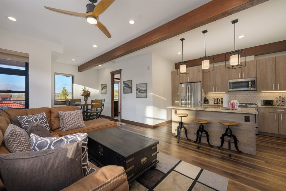 Relax in your stylish open-concept living space with exposed beams, modern kitchen, and cozy seating perfect for unwinding after adventures.