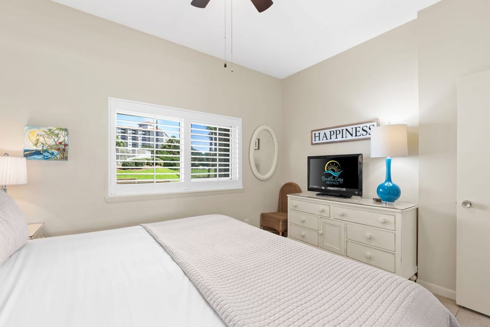Guest king bedroom with crisp linens, cozy seating, and a flat-screen TV for relaxation.
