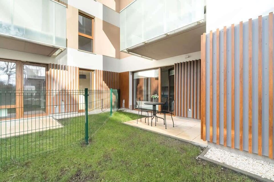 A modern building courtyard with a green lawn, patio seating, and wooden panel accents.

