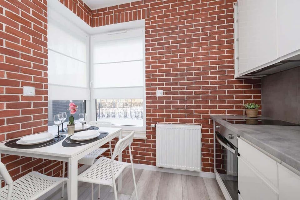 A functional kitchen and dining area with an industrial-style brick wall and modern white cabinets, providing a perfect blend of style and practicality.
