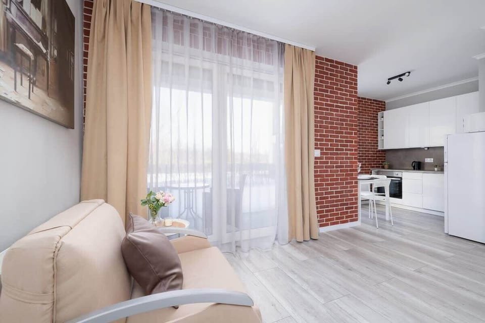 A stylish living room with a large window, an elegant sofa, and an exposed brick wall enhancing the apartment’s aesthetic appeal.
