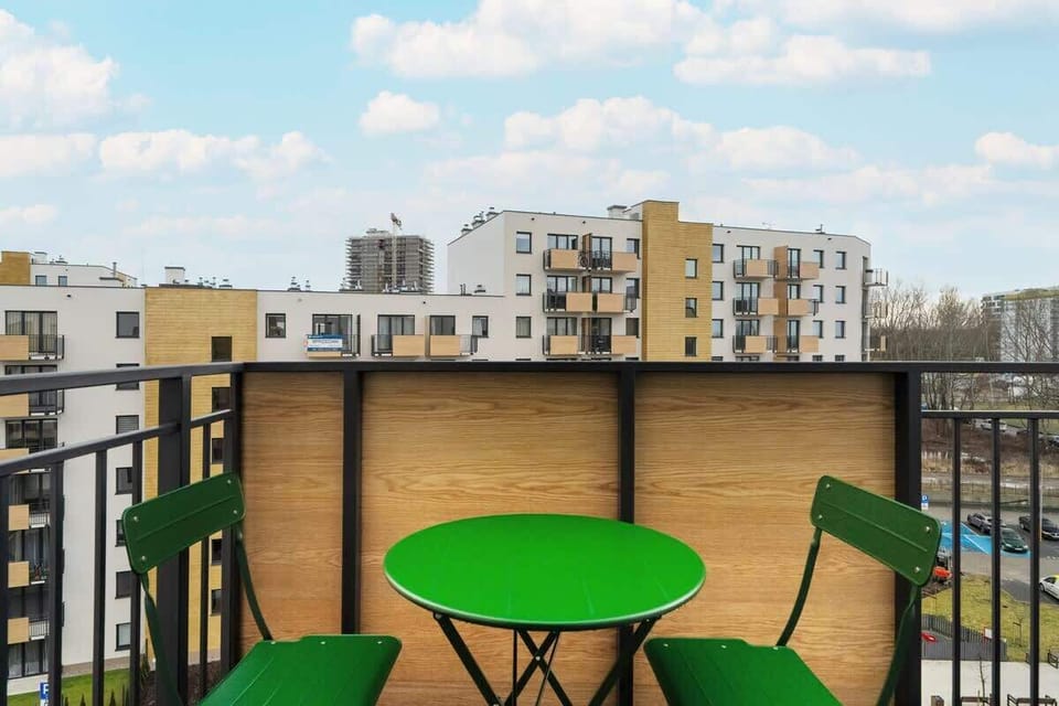 A balcony space with a round green table and matching chairs, offering a view of the surrounding urban landscape.
