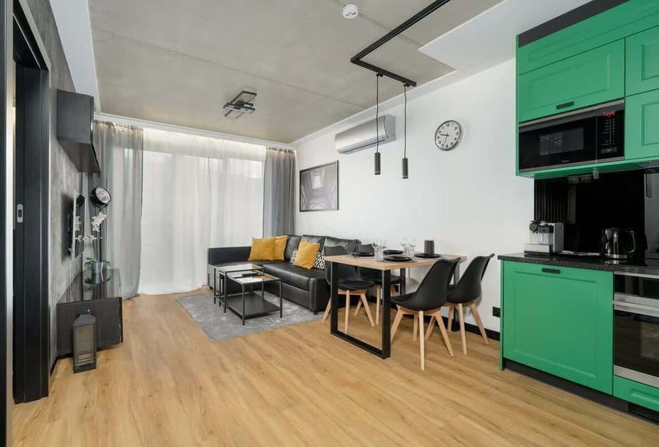 A wider view of the open-concept layout, capturing the green kitchen units, a comfortable seating area, and warm wooden floors.
