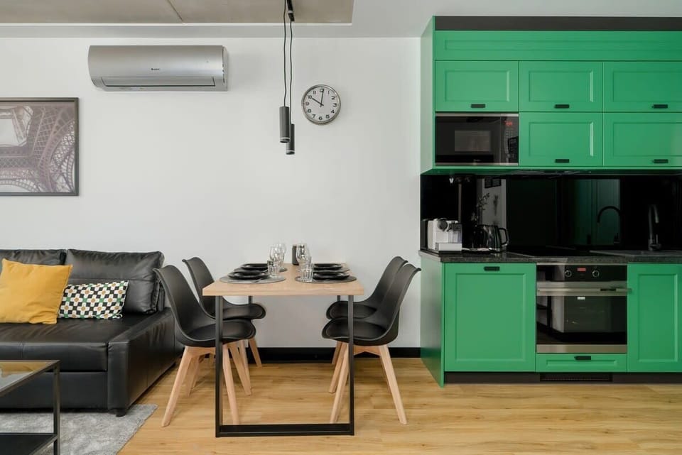 Another angle of the living space, highlighting a black sofa, the green kitchen cabinetry, and a compact dining table.

