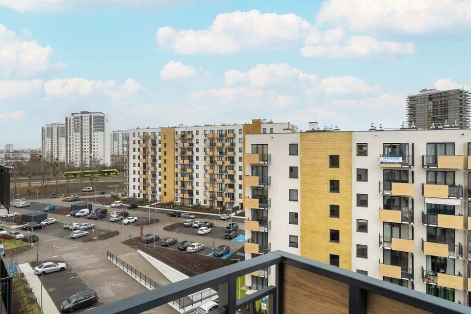 A balcony view overlooking a large residential complex with multiple apartment buildings and a spacious parking area.

