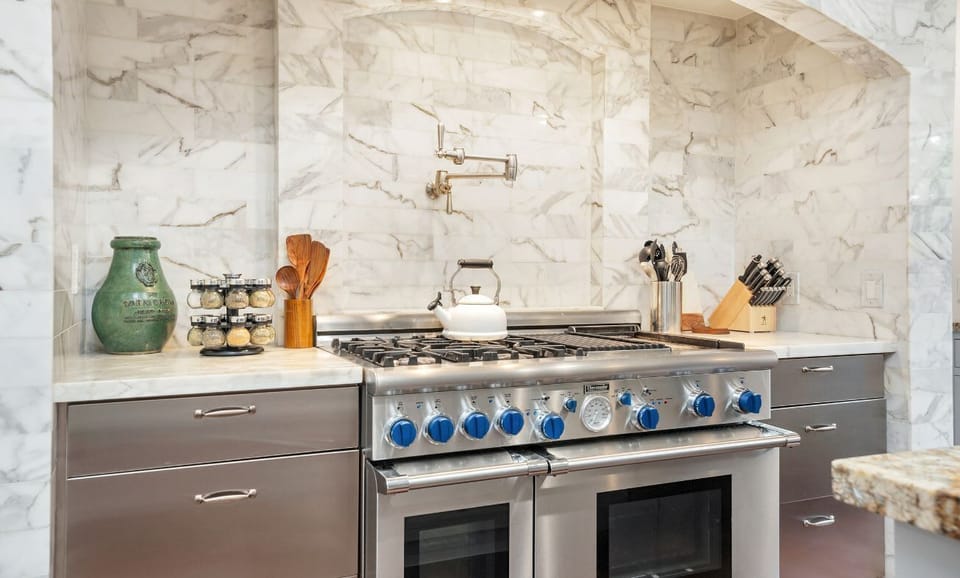 Modern kitchen with a stainless steel gas range and marble backsplash for a sleek cooking experience.