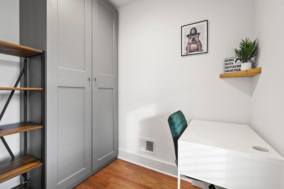 Master Bedroom Workspace-A dedicated workspace with a clean white desk and a comfortable emerald green chair provides a productive corner for remote work or study. The built-in, floor-to-ceiling gray shaker-style wardrobes offer ample storage.