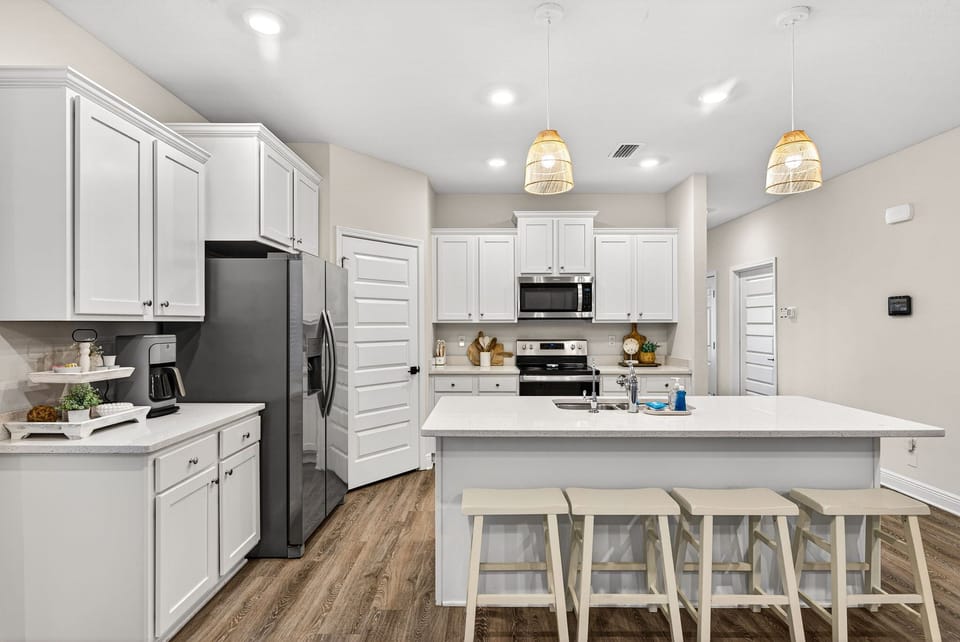 Picture yourself preparing meals in this bright, fully-equipped kitchen featuring sleek white cabinetry, modern appliances, and a spacious island with seating for gathering over morning coffee.