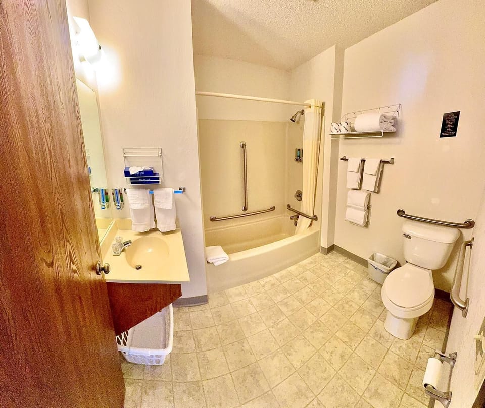 Bathroom includes sink area, mirror, fresh towels, body wash, 2-in-1 shampoo and conditioner, and body wash. This room has an elevated toilet and handrails in the tub and by the toilet. 