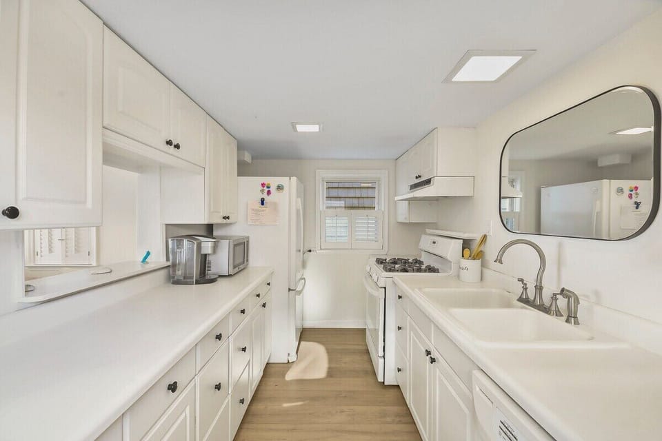 Step into our bright, all-white galley kitchen! Equipped with all the essentials—stove, fridge, toaster oven, and sink—this efficient space is perfect for preparing meals during your beach getaway. The large mirror adds a modern touch. 