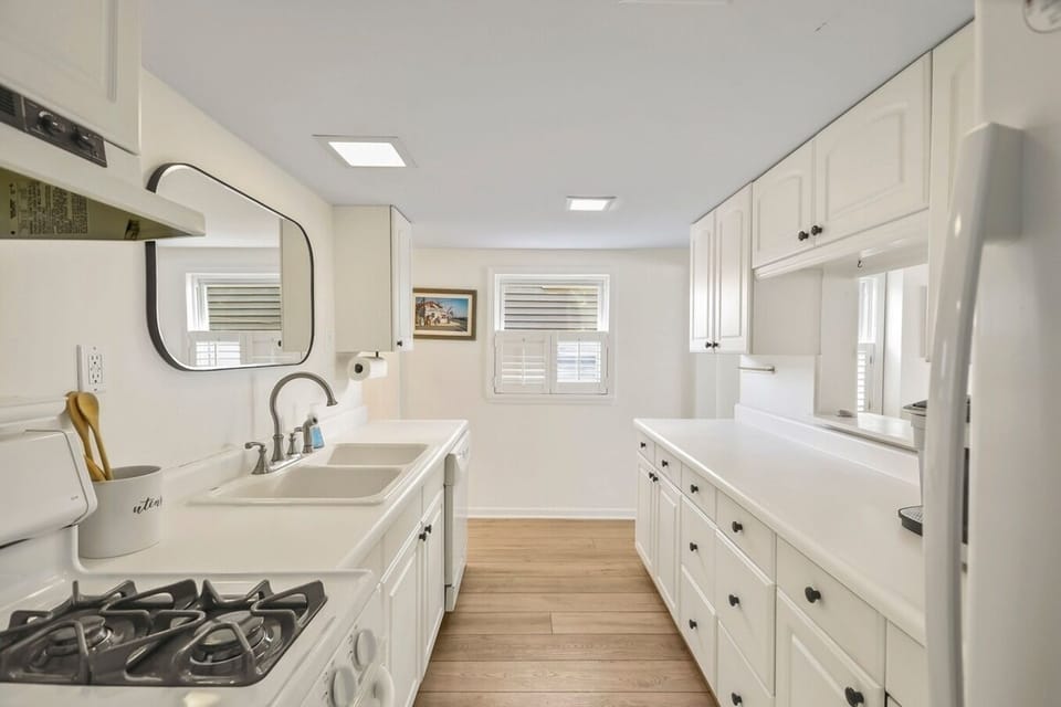 Step into our bright, all-white galley kitchen! Equipped with all the essentials—stove, fridge, toaster oven, and sink—this efficient space is perfect for preparing meals during your beach getaway. The large mirror adds a modern touch. 