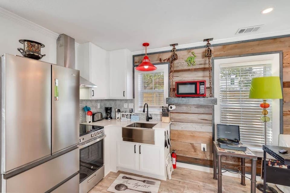 - Kitchen with a modern stainless steel fridge, stove, & a deep farmhouse sink - Unique mix of wood paneling, bright red pendant light, & quirky decor adds charm - Well equipped space for cooking and entertaining, with plenty of light and personality