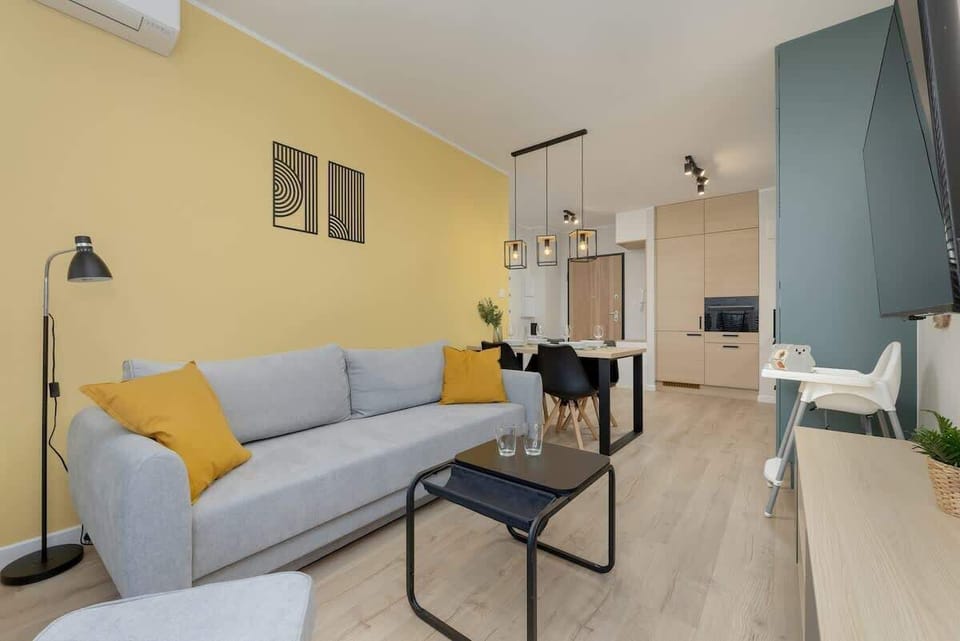 Living room with a light blue sofa, a coffee table, and large artwork on the wall, featuring a yellow accent wall and large windows.