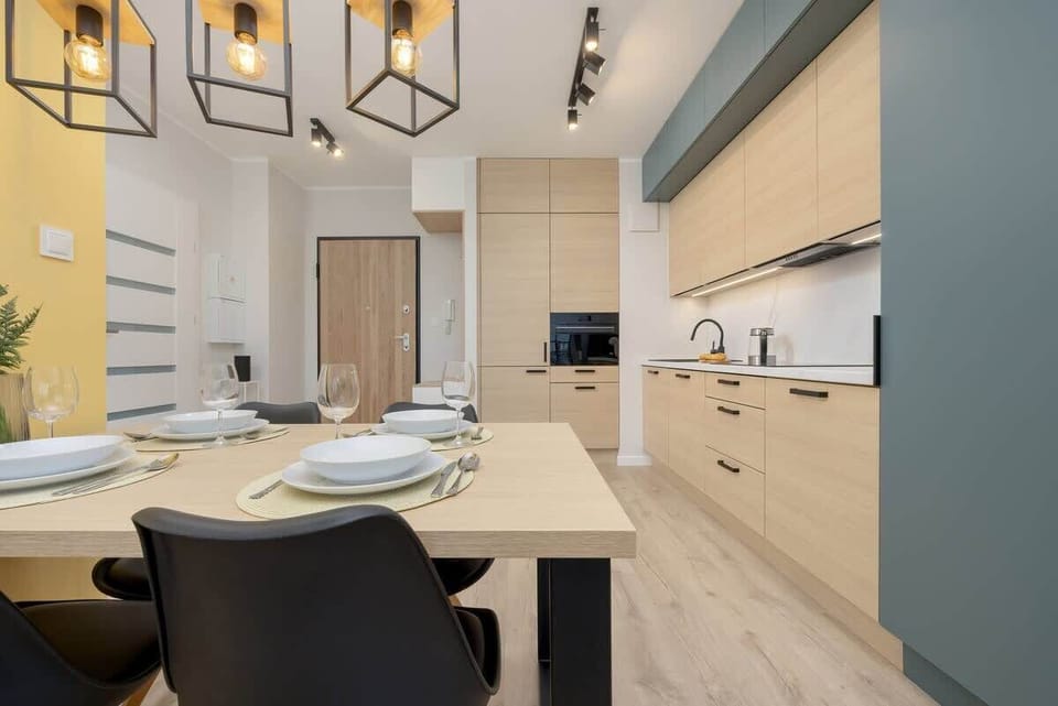Dining area featuring a light wooden table, black chairs, and a yellow wall in the background, with modern lighting fixtures.