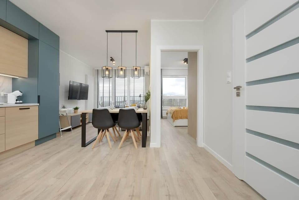 Dining area featuring a light wooden table, black chairs, and a yellow wall in the background, with modern lighting fixtures.