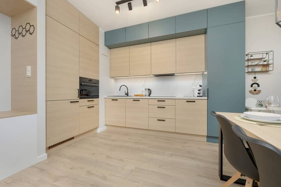 Kitchenette with light wood cabinets, a white countertop, and teal backsplash, with an open and airy feel.