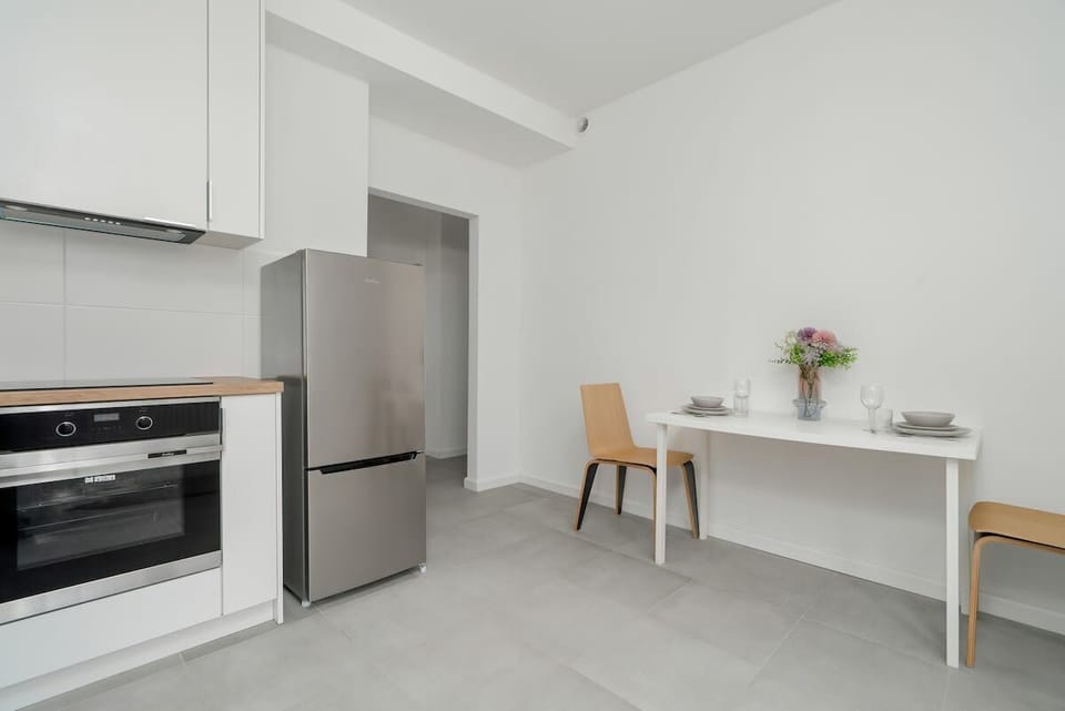A kitchen and dining area with a small wooden table, white cabinets, and stainless steel appliances.

