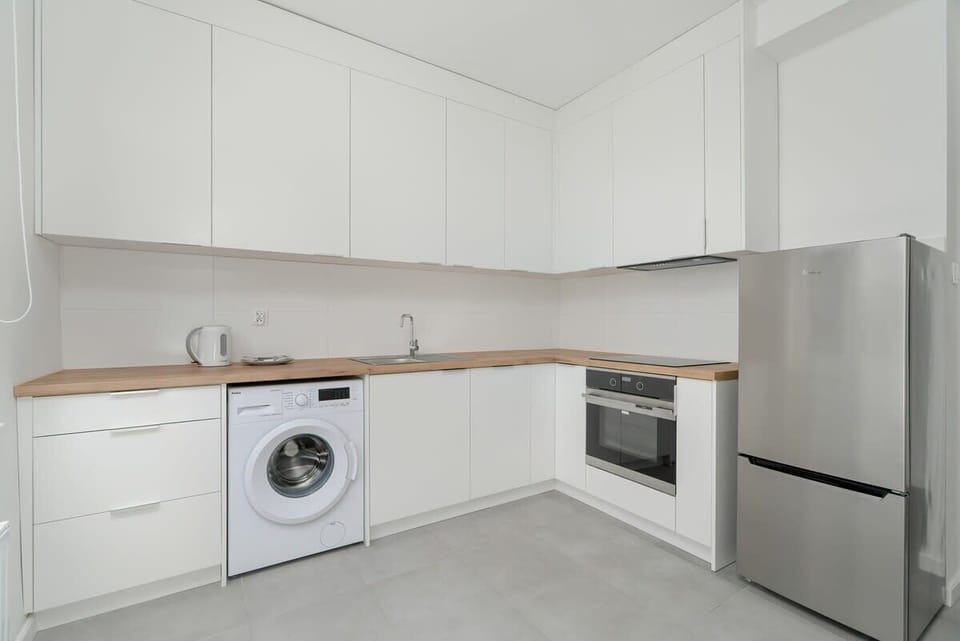 A modern kitchen with white cabinetry, built-in appliances, and a washing machine integrated under the counter.
