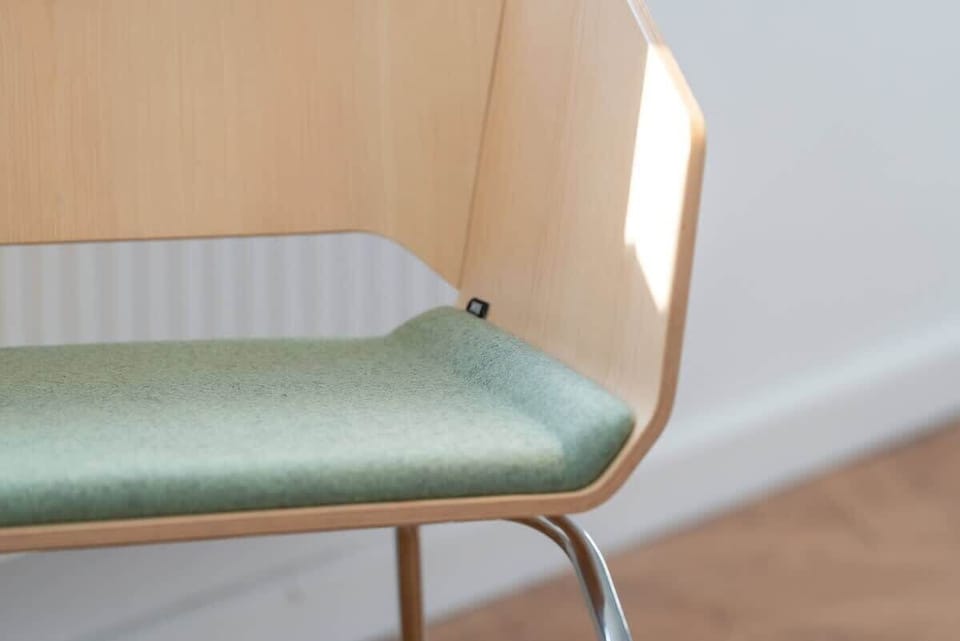 A detailed shot of a chair with a natural wood finish and a soft green seat cushion.
