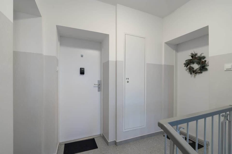 A clean and well-lit apartment hallway with white doors and a decorative wreath.
