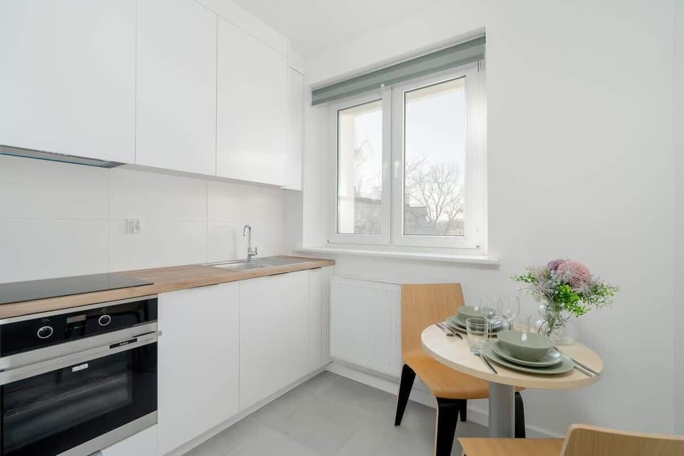 A sleek white kitchen with a wooden countertop, a built-in oven, and a cozy dining area by the window.

