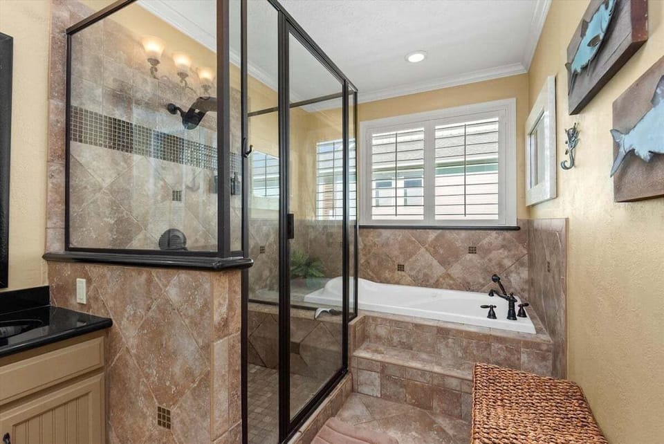 Detailed view of the primary bathroom's glass walk-in shower, tiled soaking tub, granite vanity and large windows with plantation shutters.