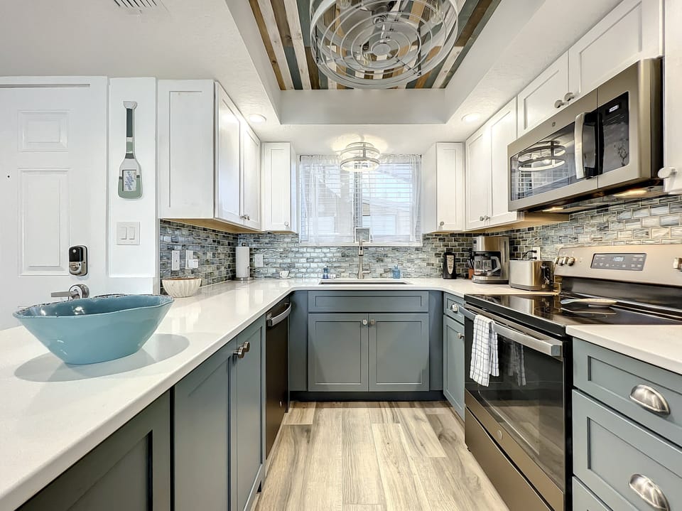 This chic kitchen boasts modern appliances, stylish cabinetry, and a unique wood-paneled ceiling, combining sleek functionality with coastal charm for an ideal culinary space.