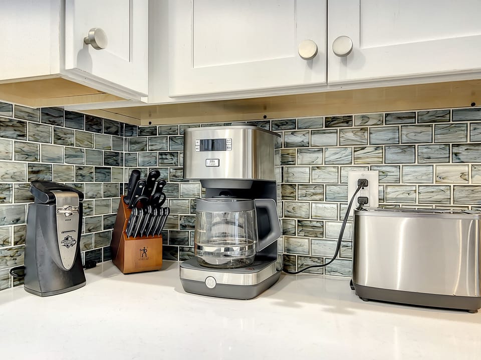 This sleek kitchen corner is equipped with a coffee maker, toaster, and knife set, ideal for preparing morning meals in a stylish space featuring a beautiful glass tile backsplash.