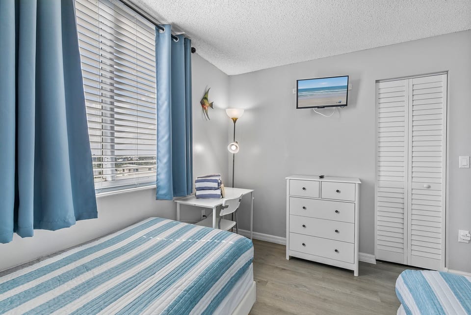 This cozy twin bedroom features a soothing coastal-inspired design with soft blue and white striped bedding and matching curtains that frame large windows, filling the room with natural light.