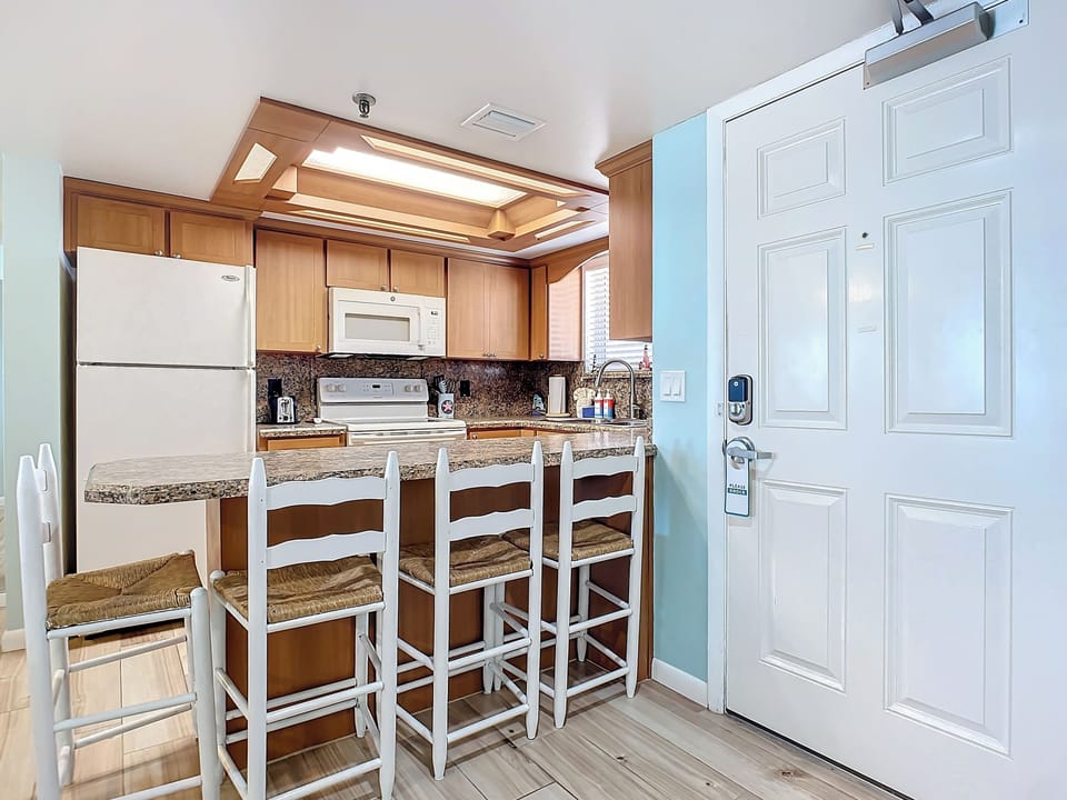 Fully equipped kitchen featuring granite counters, wood cabinetry, and a breakfast bar with seating for four. Ideal for cooking and gathering.