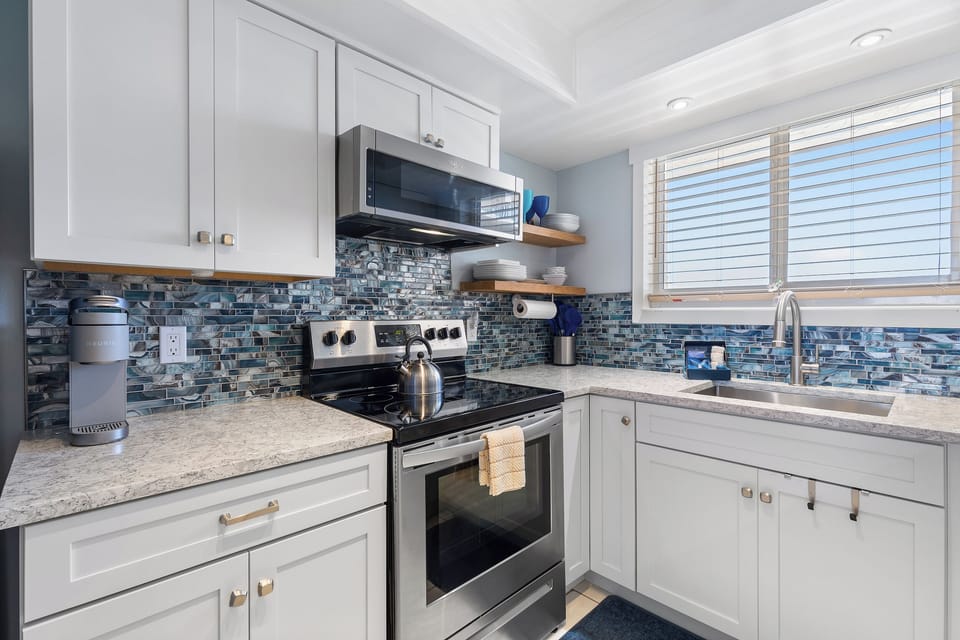 A kitchen with coastal charm, featuring glass-tile backsplash, quartz countertops, and plenty of natural light.
