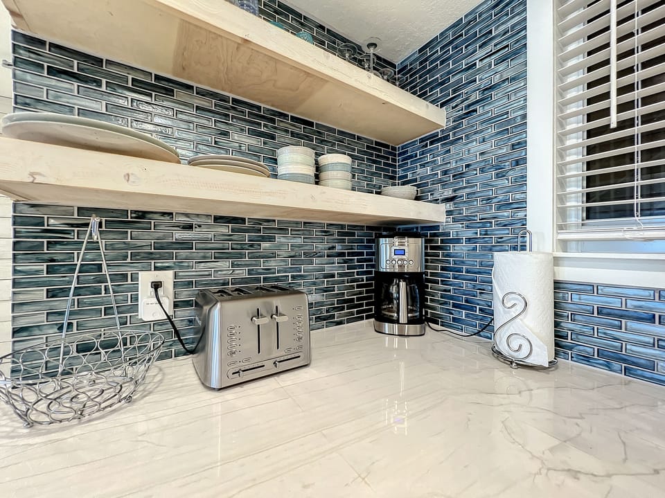 A stylish countertop with a blue-tiled backsplash, wooden shelves, and essentials like a toaster and coffee maker. A cozy, functional nook for morning routines.
