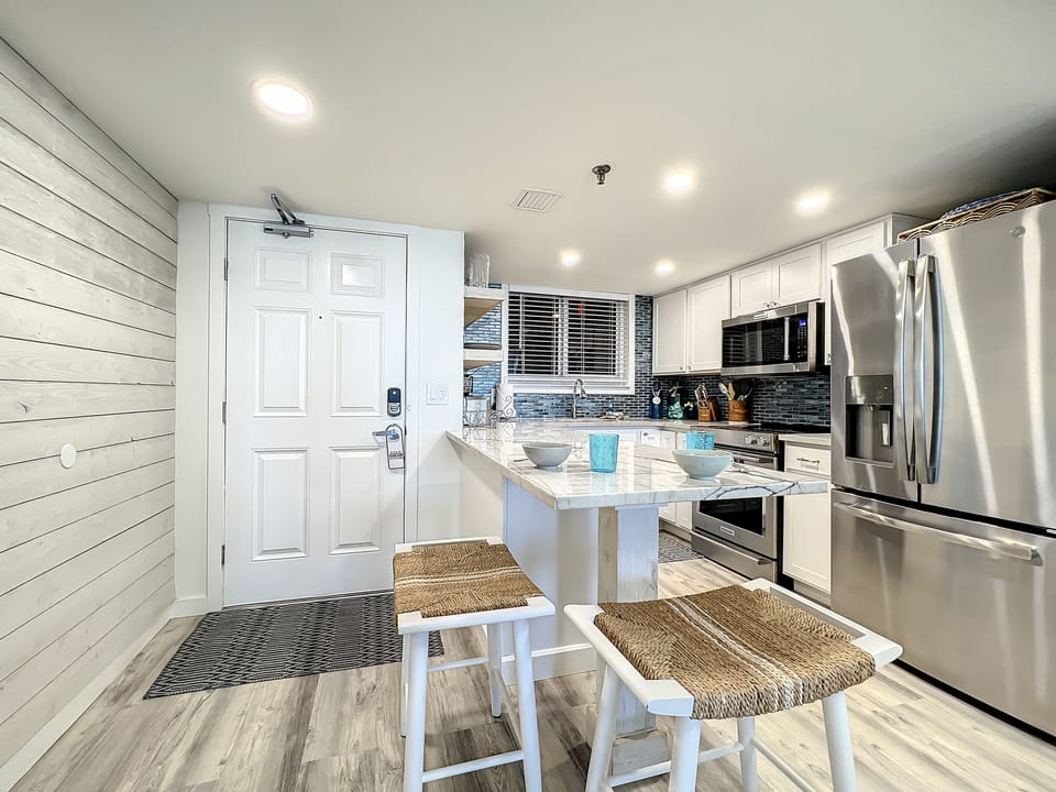 A sleek, fully equipped kitchen with stainless steel appliances, a marble island, and cozy seating. Perfect for creating meals and enjoying a relaxed coastal vibe.