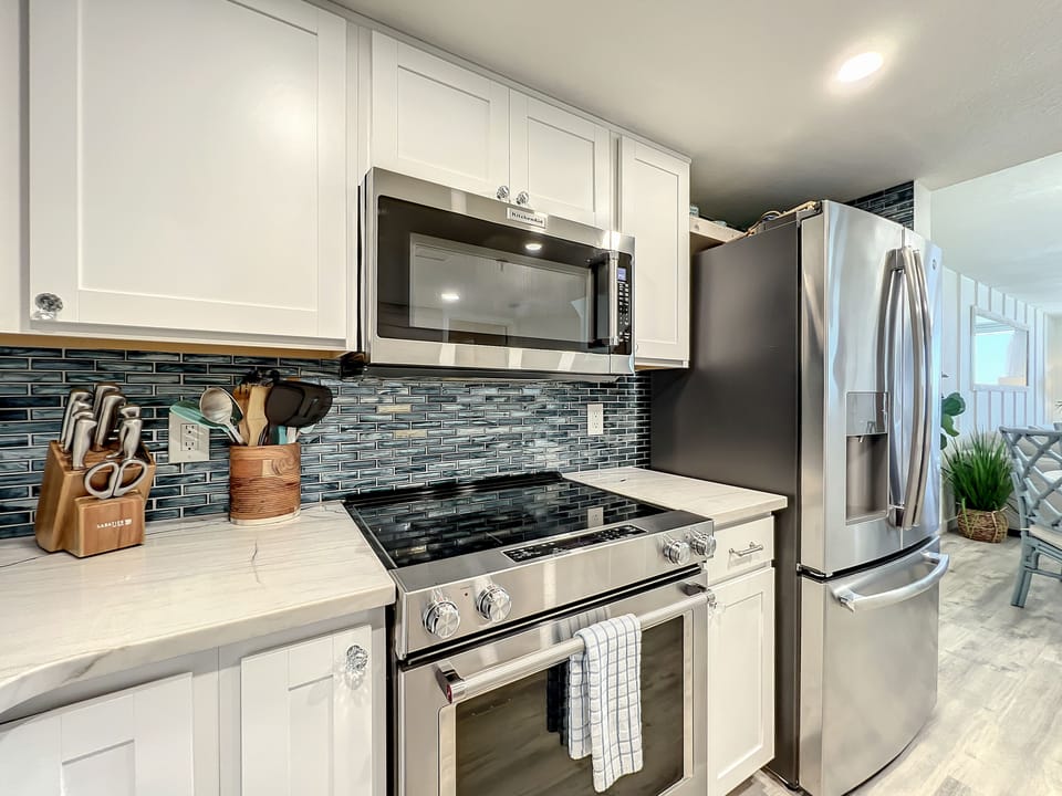 A sleek stainless-steel oven and refrigerator, complemented by a blue-tiled backsplash, white cabinetry, and a well-organized knife set. Ideal for preparing meals in style.