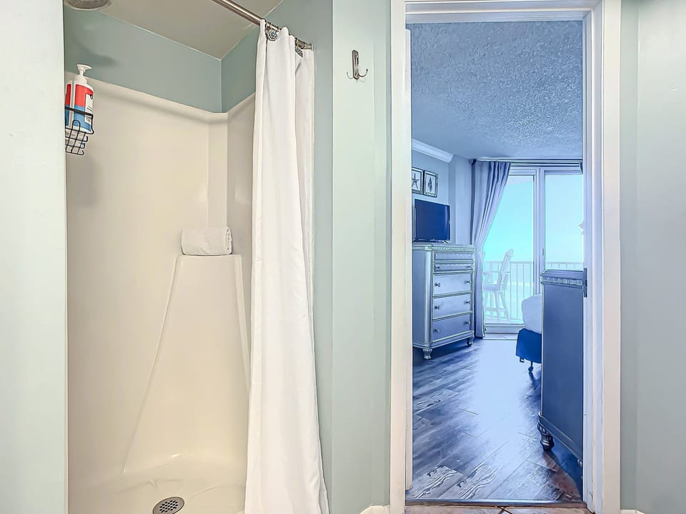 Practical walk-in shower adjacent to a serene bedroom with balcony access and ocean views.