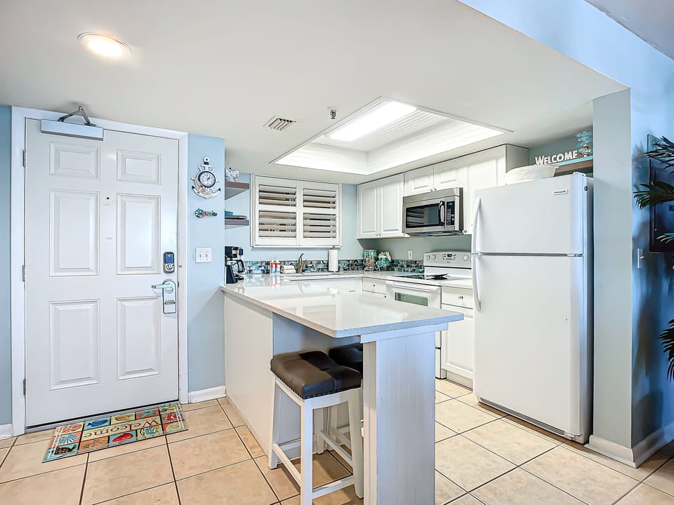 Bright kitchen with ample counter space, modern appliances, and charming coastal details by the entrance.