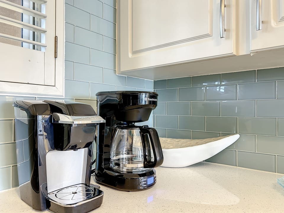 A sleek coffee station featuring a drip coffee maker and single-serve machine, set against a stylish backsplash. Perfect for enjoying a fresh cup of coffee during your stay.