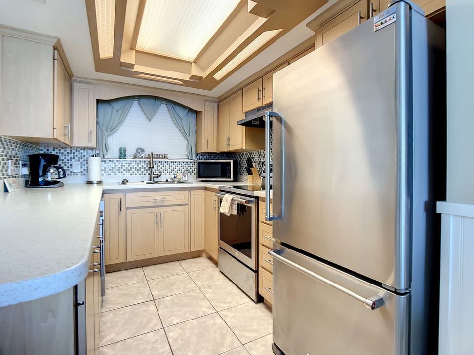 This modern kitchen offers ample counter space, stainless steel appliances, and a stylish mosaic backsplash. With a well-lit ceiling and cozy layout, it's perfect for preparing meals and enjoying your beachside stay.