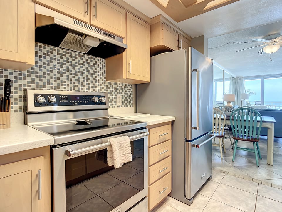 This sleek kitchen features stainless steel appliances, including a spacious refrigerator and an electric stove with a stylish mosaic backsplash. Perfect for cooking your favorite meals while enjoying the open-concept design and ocean views.